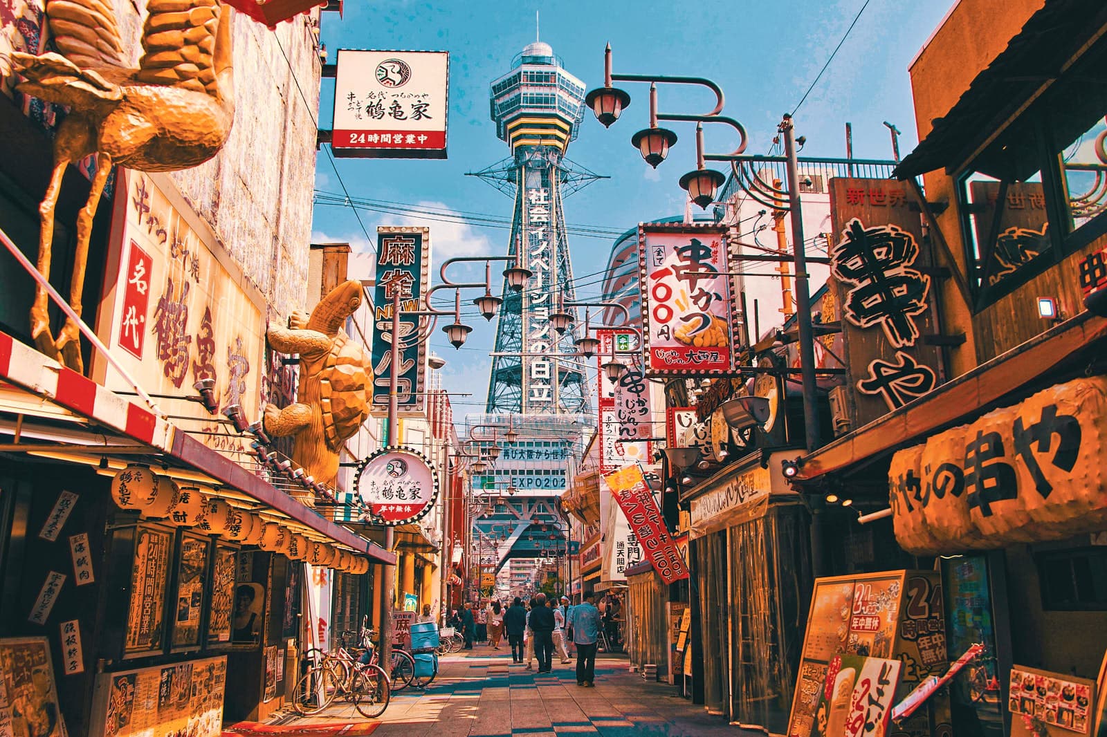 Osaka city skyline with elevated railway lines, dense urban streets, and neon signs at dusk